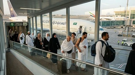 معتمرون ومسافرون مسلمون أثناء الصعود إلى طائرة الخطوط السعودية في مطار جدة وسط أجواء روحانية وتنظيم حديث.